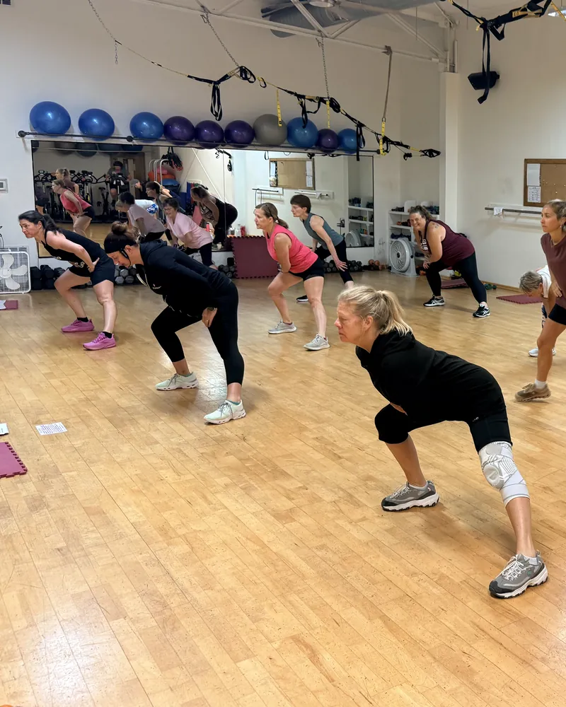 A group fitness class at Sara's Health and Fitness &mdash; members working through a standing stretch together on the studio floor